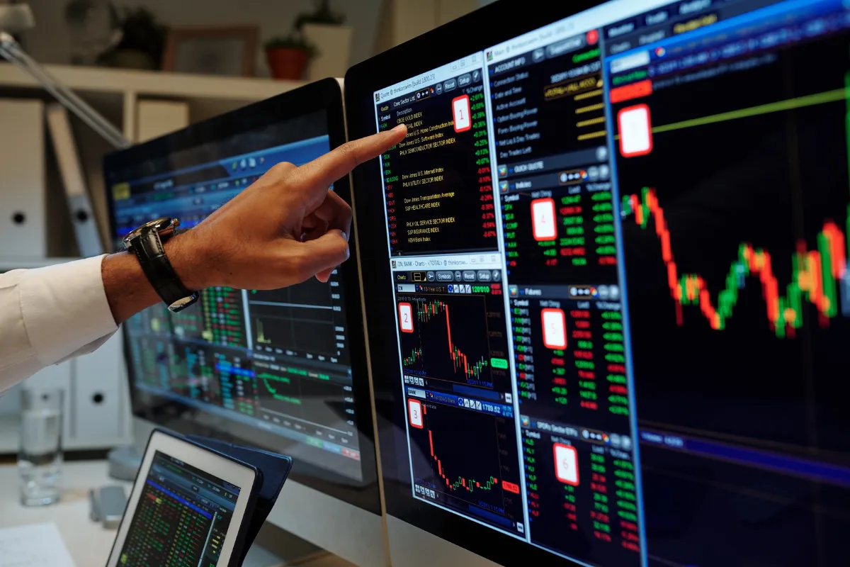 Hand pointing at trading charts on screens